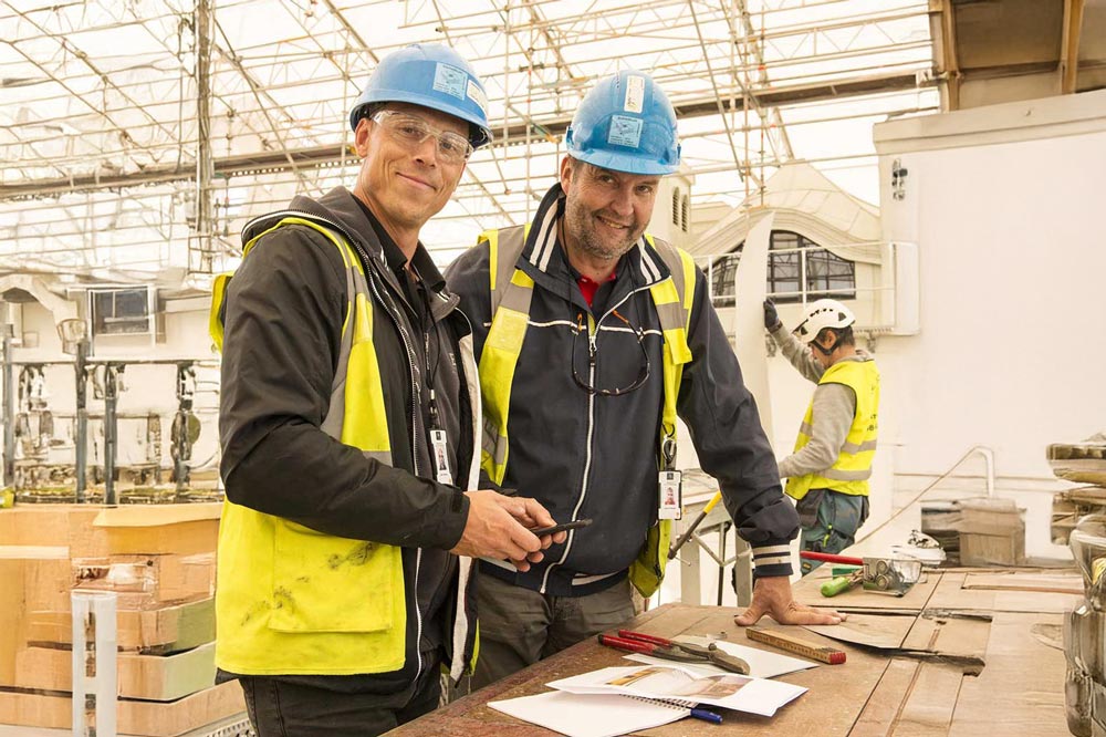 Två personer i varselvästar och blå hjälm som ler mot kameran.